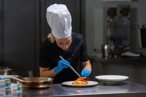 Profesionalna kuharica z modrimi nitril rokavicami pripravlja jed