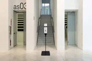 Podajalnik razkužila za roke na stojalu pred stopniščem v poslovni stavbi TTS