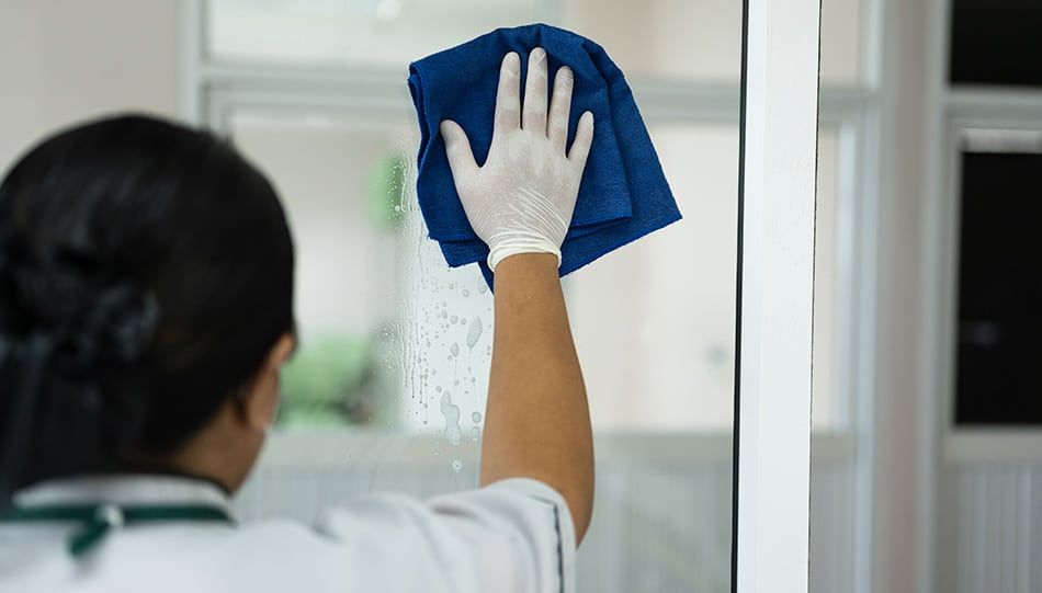 Gospa z belimi lateks rokavicami in krpo iz mikrofibre čisti steklo
