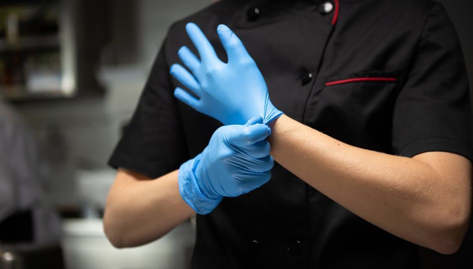 Kuhar v črni kuharski obleki z modrimi nitril rokavicami za enkratno uporabo