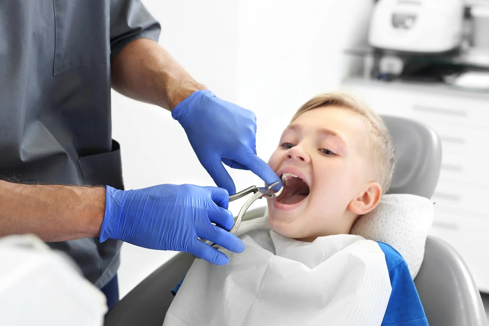 Zobozdravnik z modrimi nitril rokavicami puli zob otroku