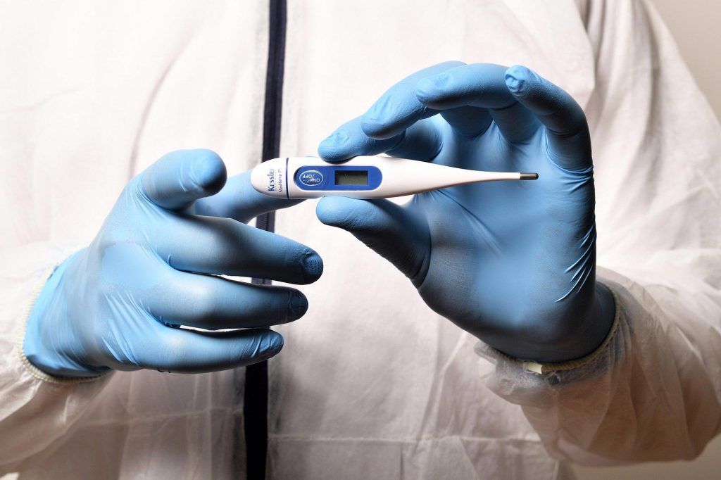 Zdravnik z modrimi nitril rokavicami drži termometer
